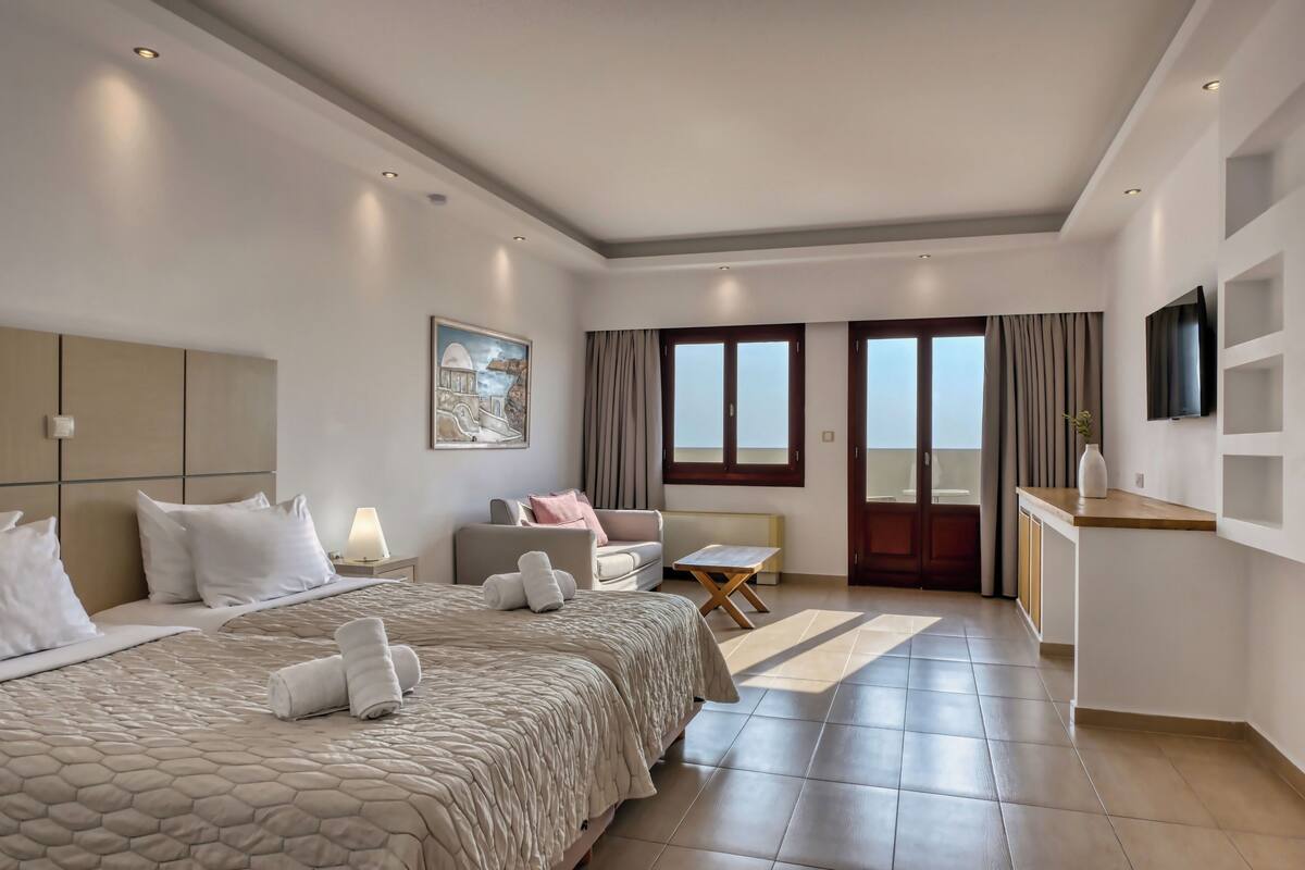 Une chambre d’hôtel avec un grand lit, un canapé, une petite table, une télévision et une fenêtre avec des rideaux.