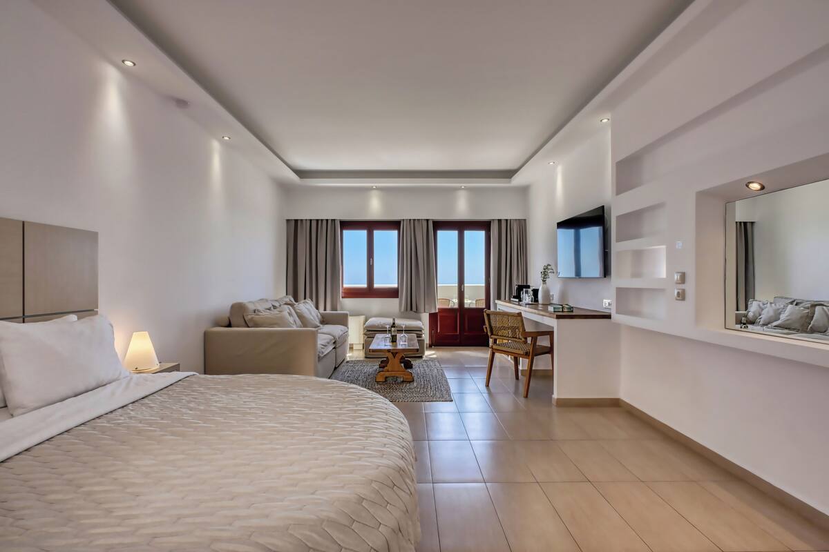 A hotel room with a large bed, a sofa, a desk, and a TV.