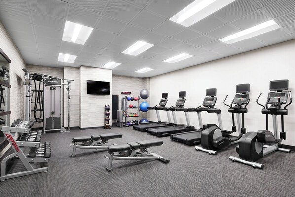 Un gimnasio con cintas de correr, elípticas y pesas libres.