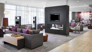A modern hotel lobby with a sectional sofa, a flat-screen TV, and a large window offering a city view. - Courtyard by Marriott Newark Downtown (Newark)