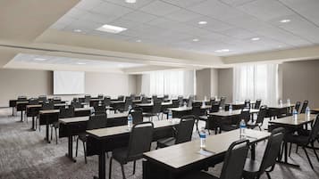 A conference room with multiple tables and chairs, equipped with water bottles, in a hotel setting.