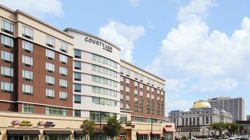 A multi-story hotel with a prominent 'Courtyard by Marriott' sign, featuring a mix of brown and beige exterior, large windows, and a central dome structure.
