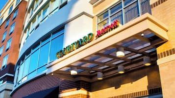 Entrada de un hotel Courtyard Marriott con fachada de vidrio, exterior de ladrillo y un cartel sobre la entrada.
