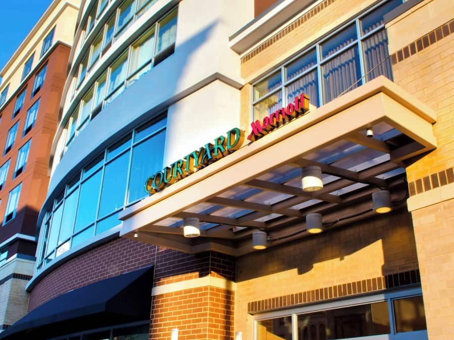Entrada de un hotel Courtyard Marriott con fachada de vidrio, exterior de ladrillo y un cartel sobre la entrada.