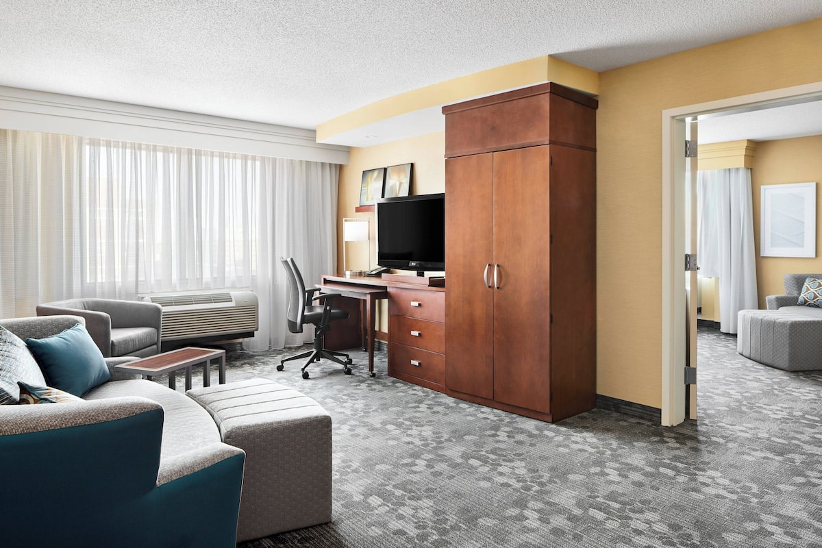 A hotel room with a sofa, a desk with a computer, a television, and a wardrobe.