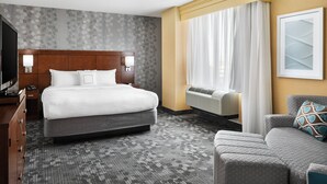A hotel room with a large bed, a desk with a lamp, a chair, a TV, and a window with curtains. - Courtyard by Marriott Newark Downtown (Newark)