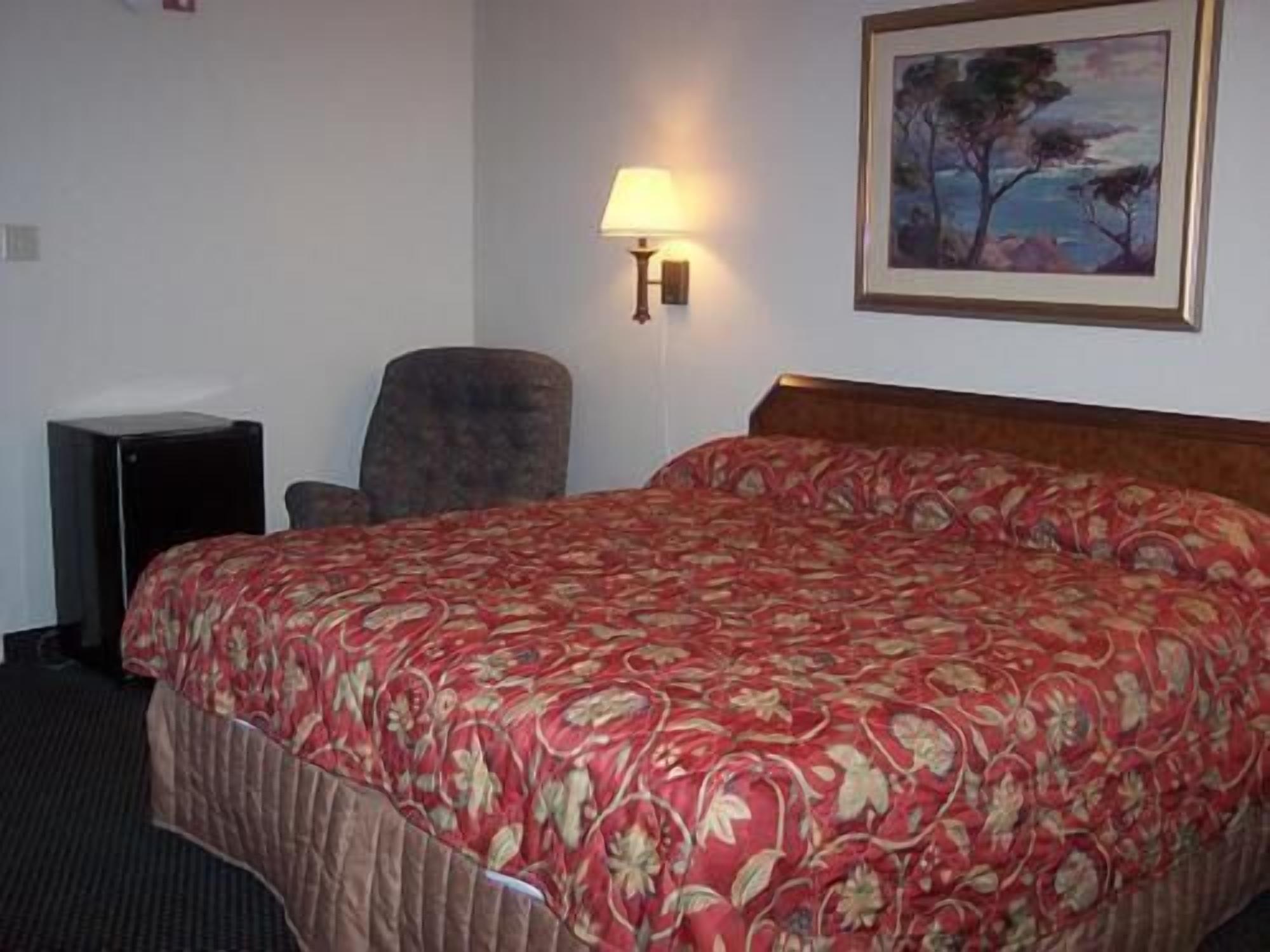 A hotel room with a large bed, a chair, a desk, and a painting on the wall.