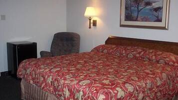 A hotel room with a large bed, a chair, a desk, and a painting on the wall.