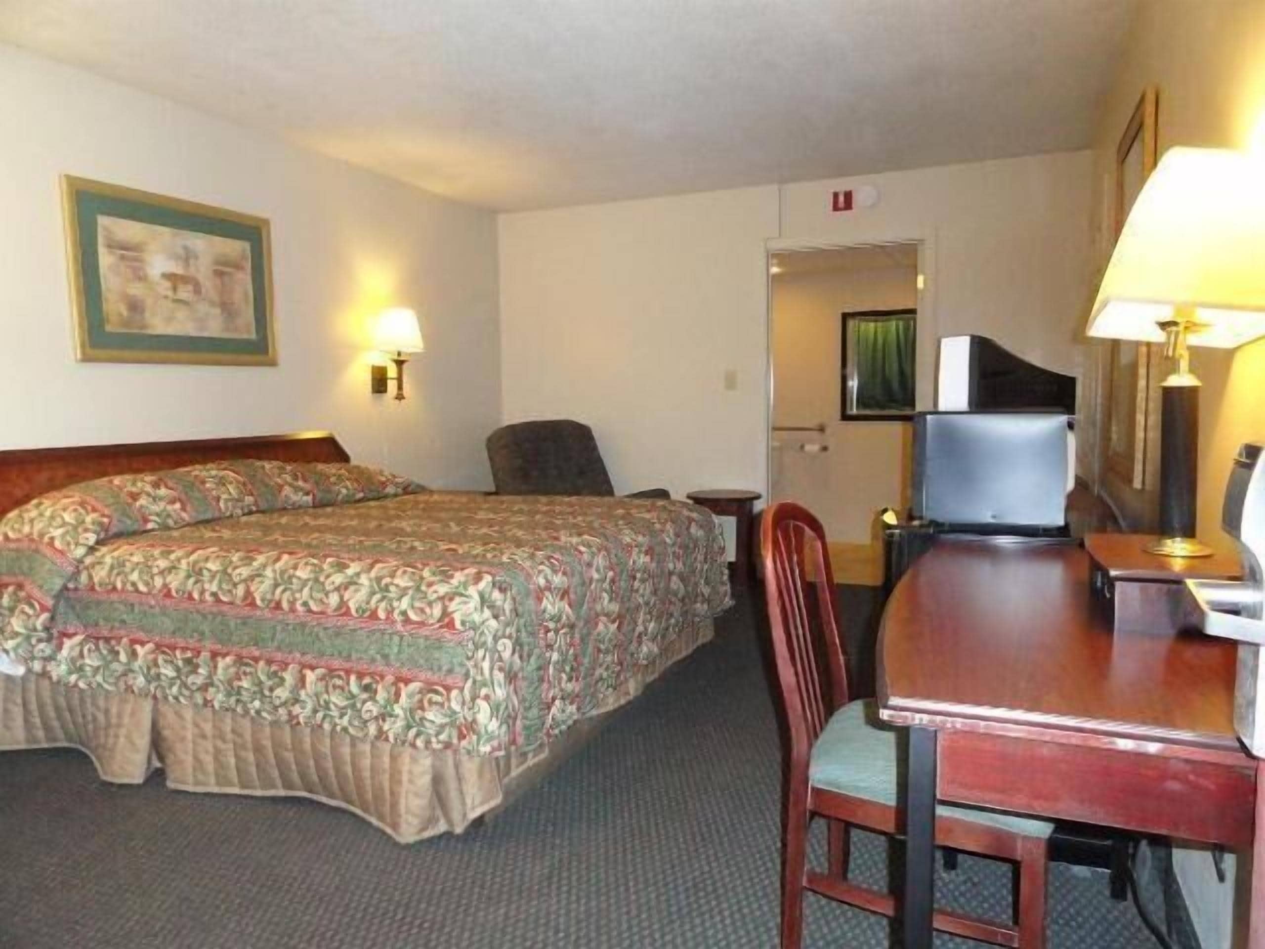 A hotel room with two beds, a desk, a chair, and a television.