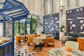 A modern interior with a blue geometric ceiling structure, a seating area with orange and grey chairs, and a patterned wall. - Grand Metropark Universal Dinosaur Town Hotel (Changzhou)