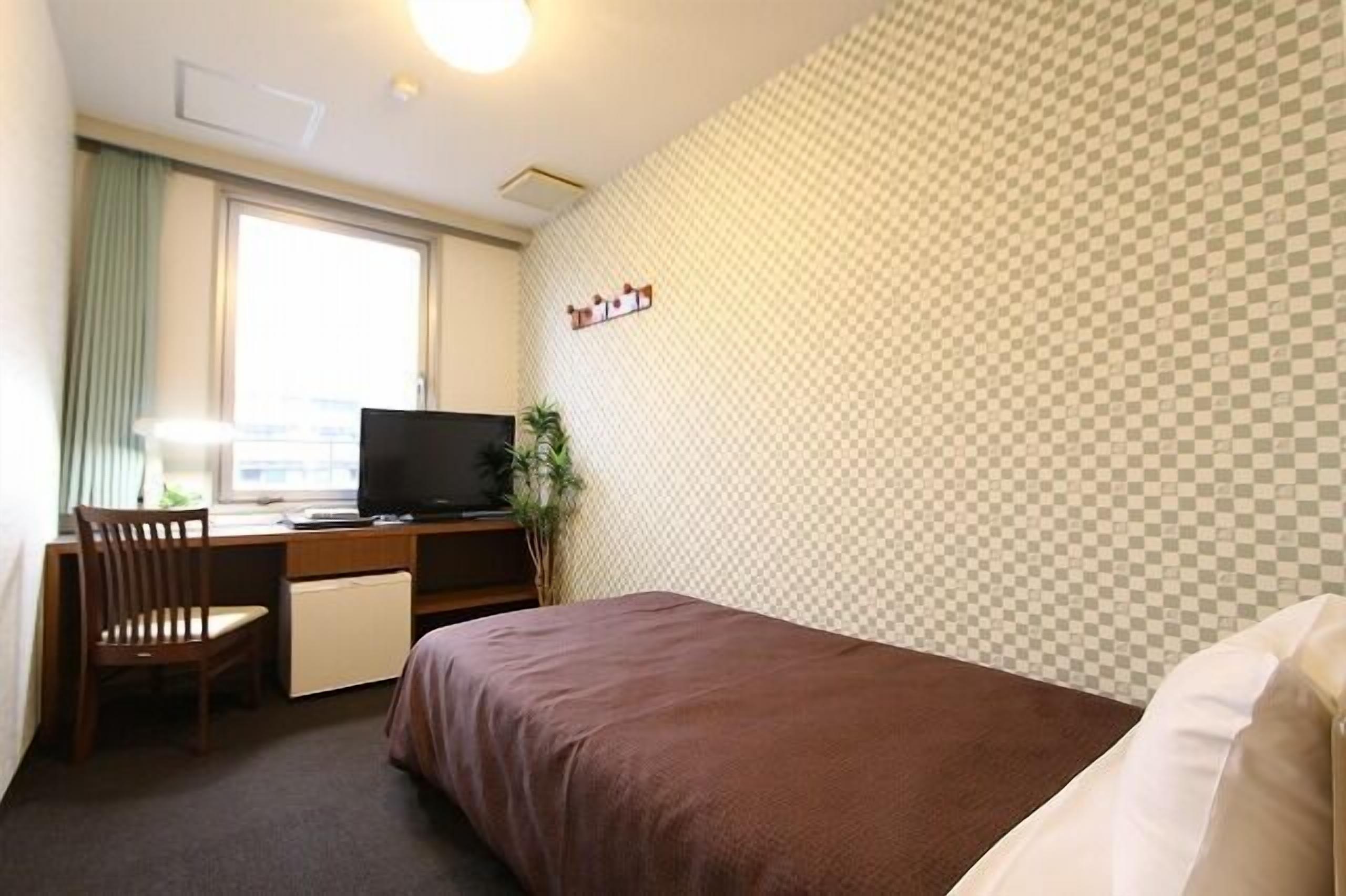 Een hotelkamer met een bed, bureau, stoel, televisie en een raam.