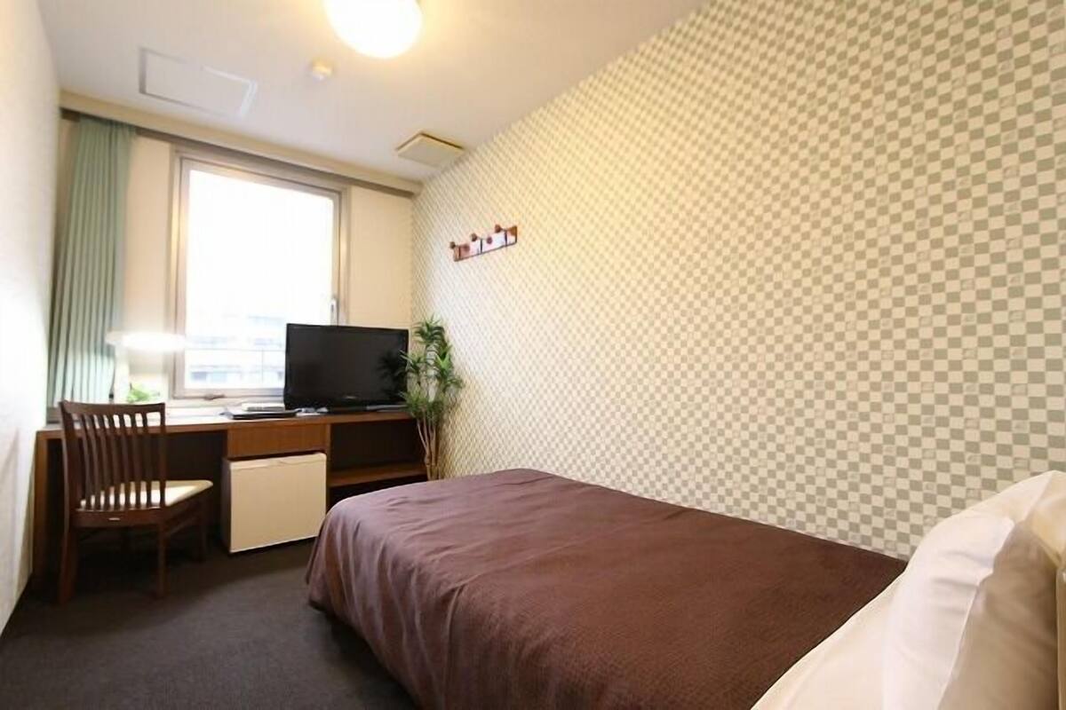Habitación de hotel con cama, escritorio, silla, televisor y ventana.
