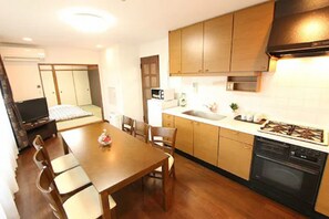 A compact kitchen with wooden cabinets, a stove, and a microwave. - HOTEL LiVEMAX Tokyo Kiba (Tokyo)