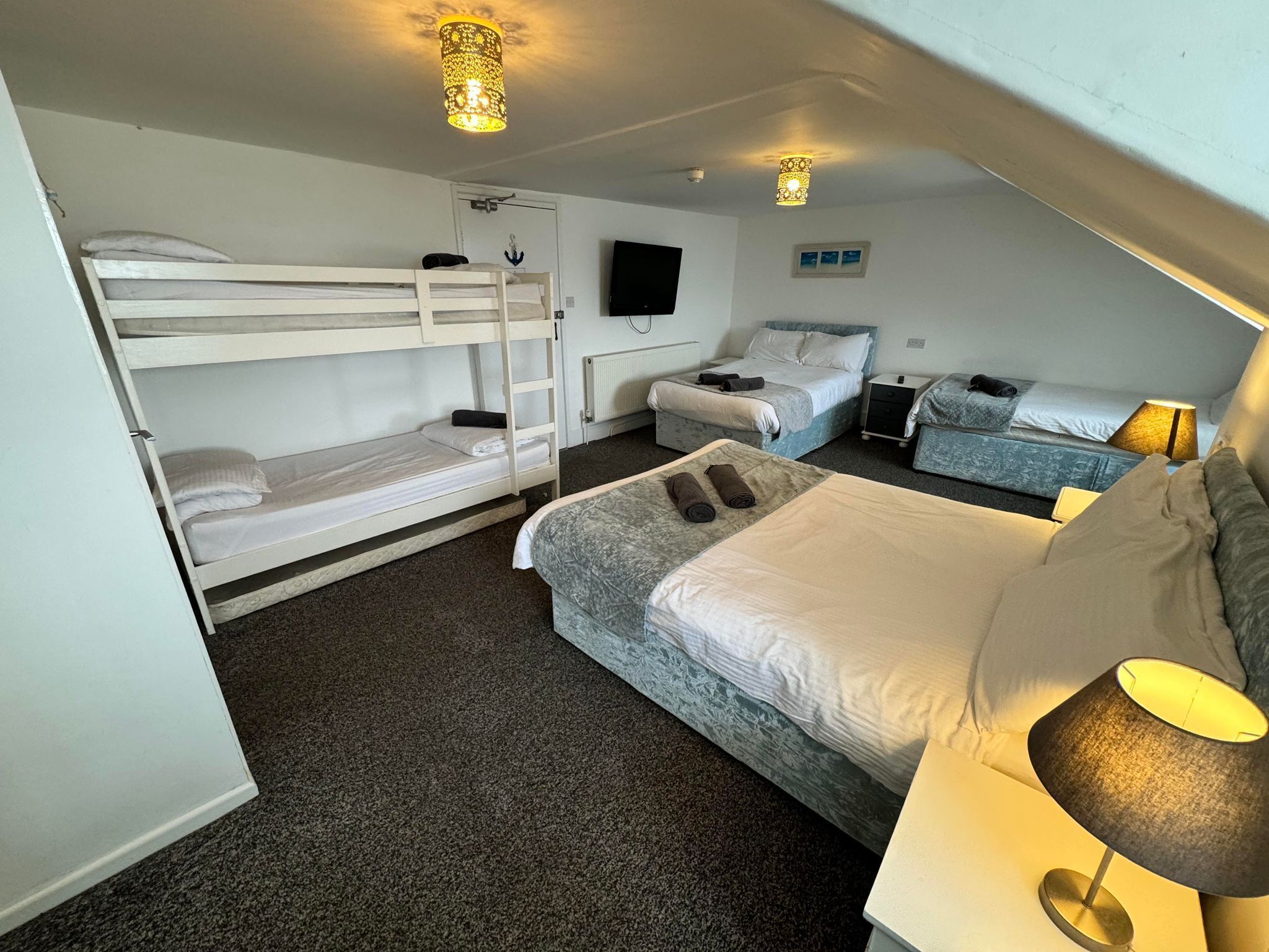 A room with bunk beds, a single bed, a TV, and a lamp.