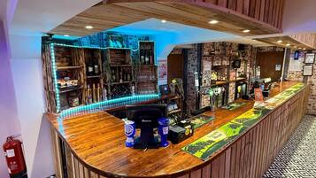 Zona de bar con mostrador de madera curvo, estanterías con botellas y suelo estampado.