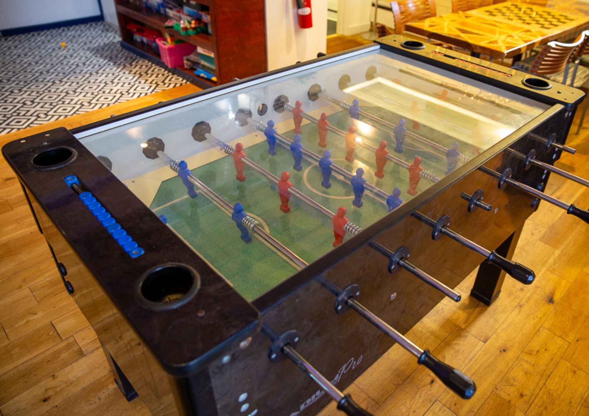 A foosball table with a glass top and metal rods, set on a wooden floor.