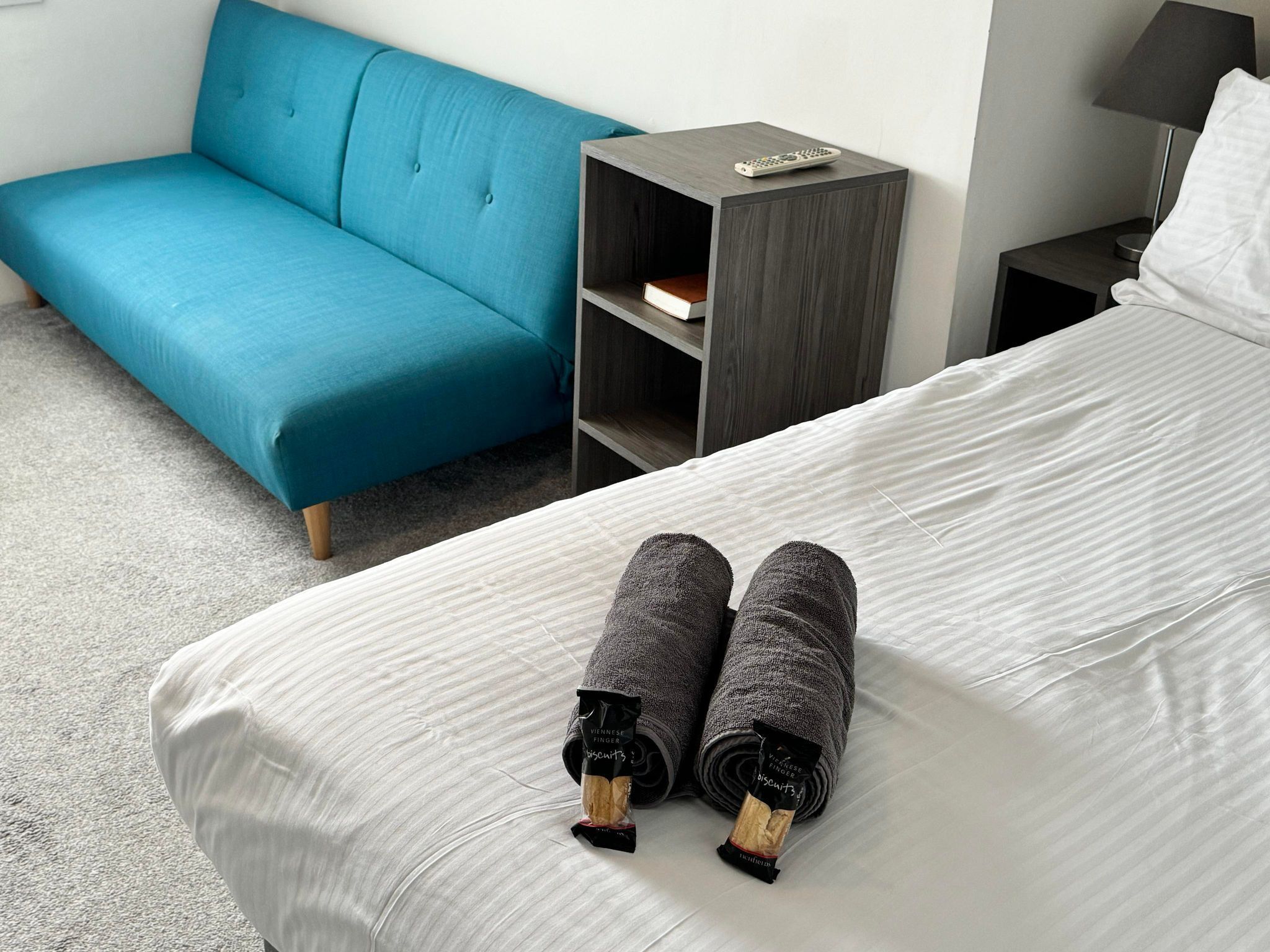 Una habitación de hotel con una cama, un sofá azul, una mesita de noche y una lámpara.