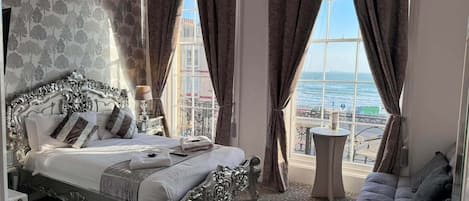 A bedroom with a large bed, a view of the sea, and a balcony with a table.