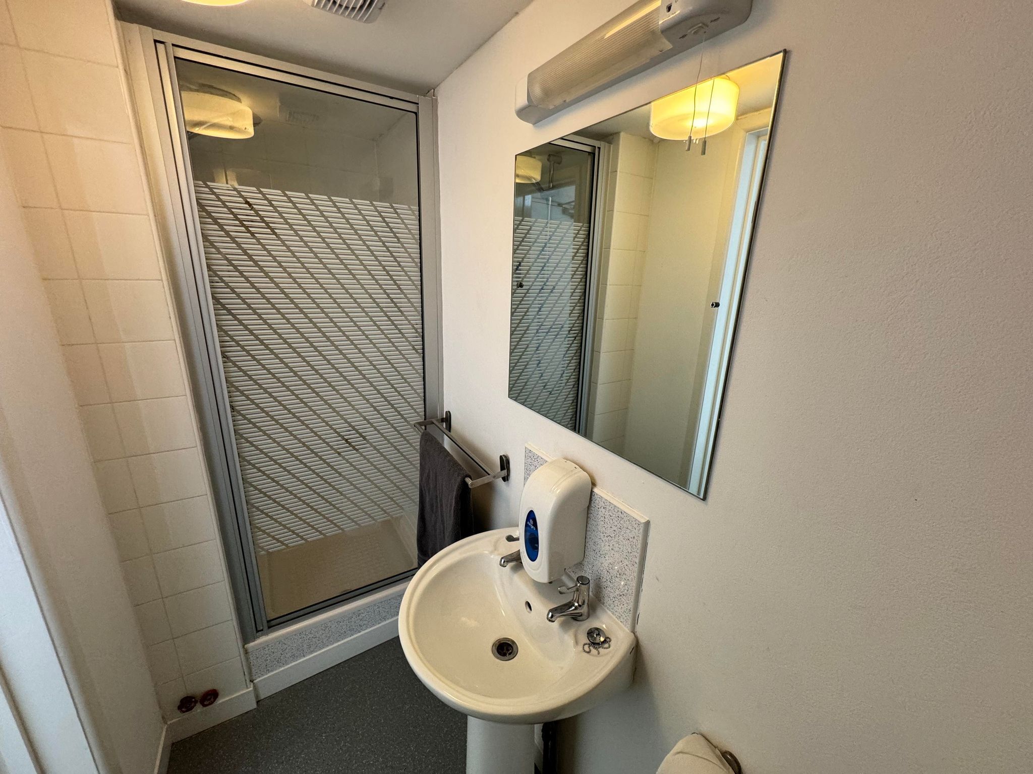 A bathroom with a glass shower door, a sink with a mirror above it, and a towel rack.