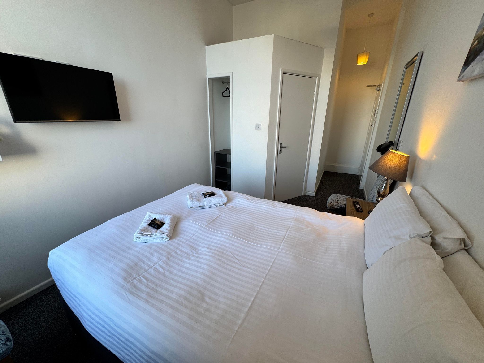 Una camera d'albergo con un grande letto, una TV a schermo piatto montata a parete, una lampada da comodino e una porta che dà su un bagno.