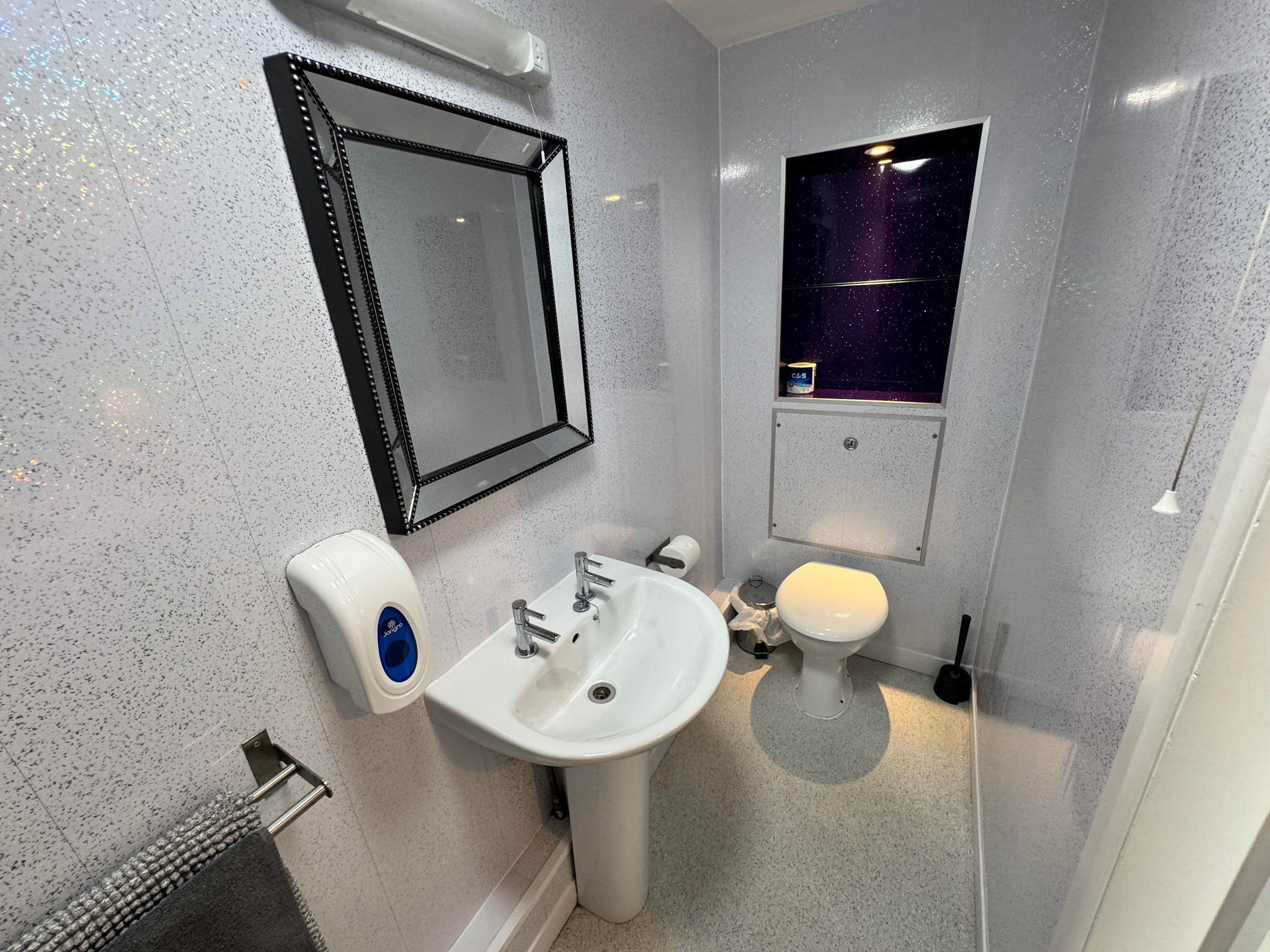 A bathroom with a white sink, a toilet, a mirror, and a small window with a starry view.