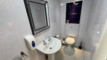 A bathroom with a white sink, a toilet, a mirror, and a small window with a starry view.