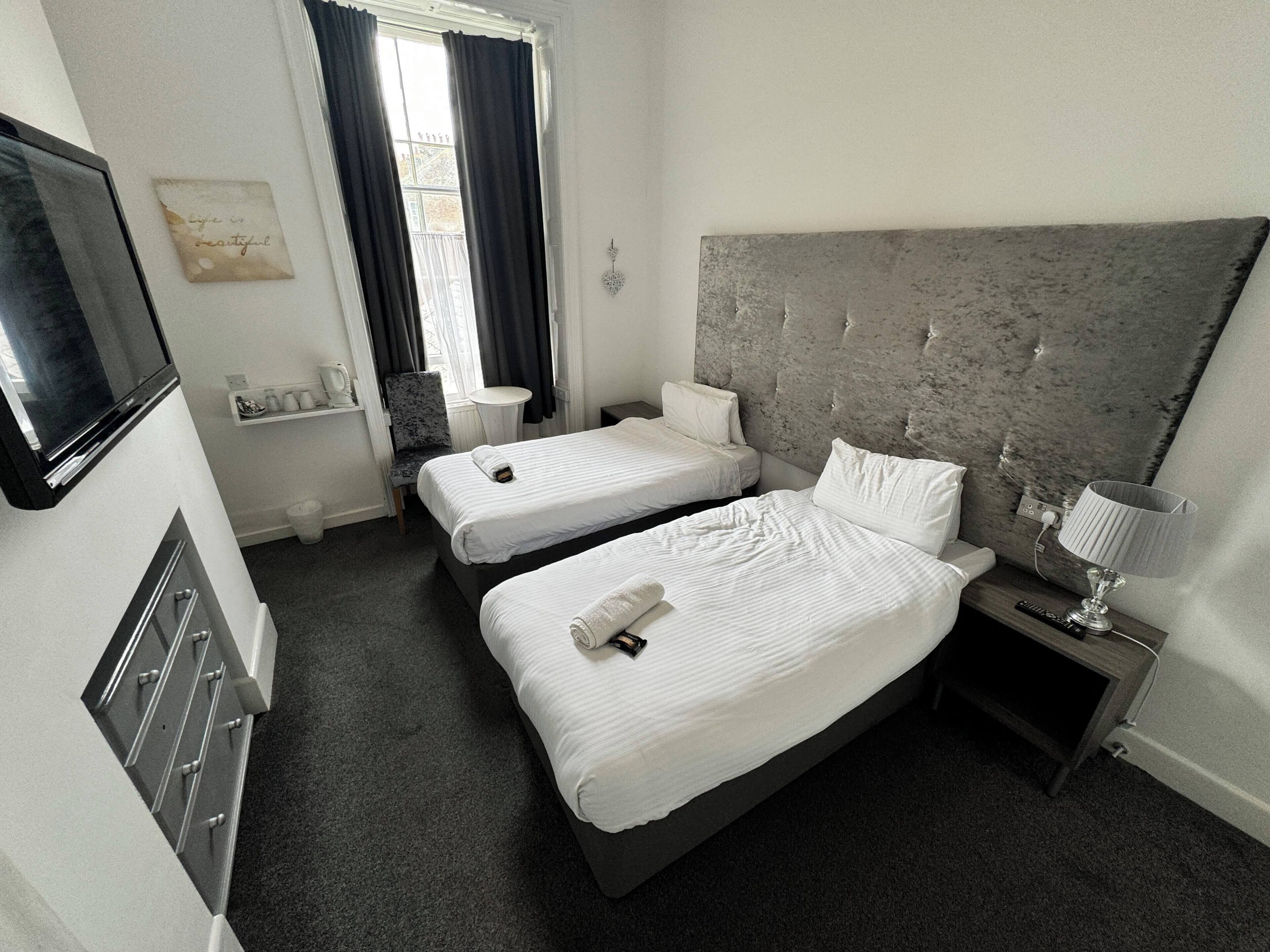 A hotel room with two single beds, a small table, a chair, a TV, and a decorative wall piece.