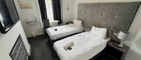 A hotel room with two single beds, a small table, a chair, a TV, and a decorative wall piece.