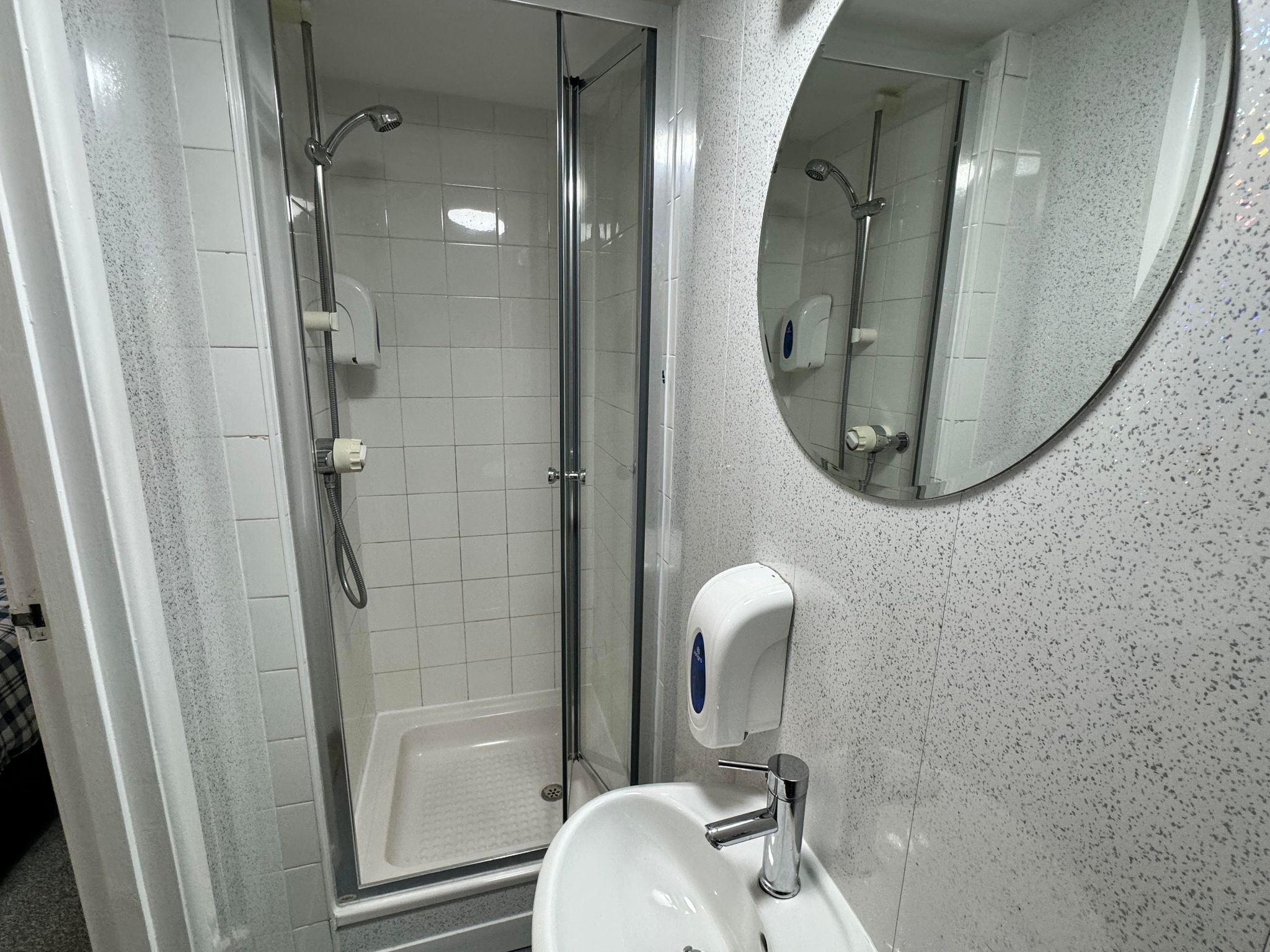 A bathroom with a glass-enclosed shower, a sink with a soap dispenser, and a round mirror.
