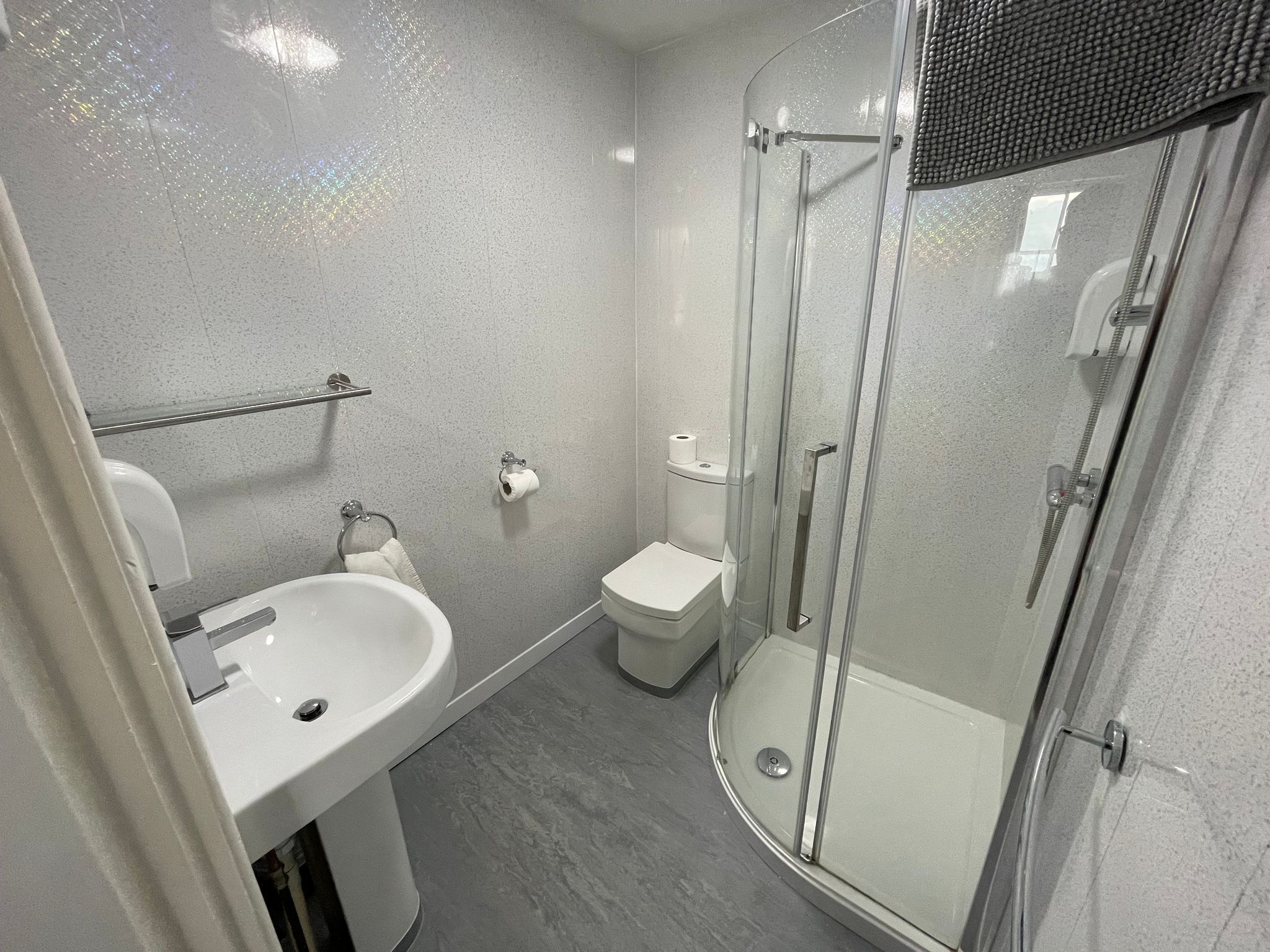 Et moderne badeværelse med en glasafskærmet brusekabine, en hvid vask og et toilet.