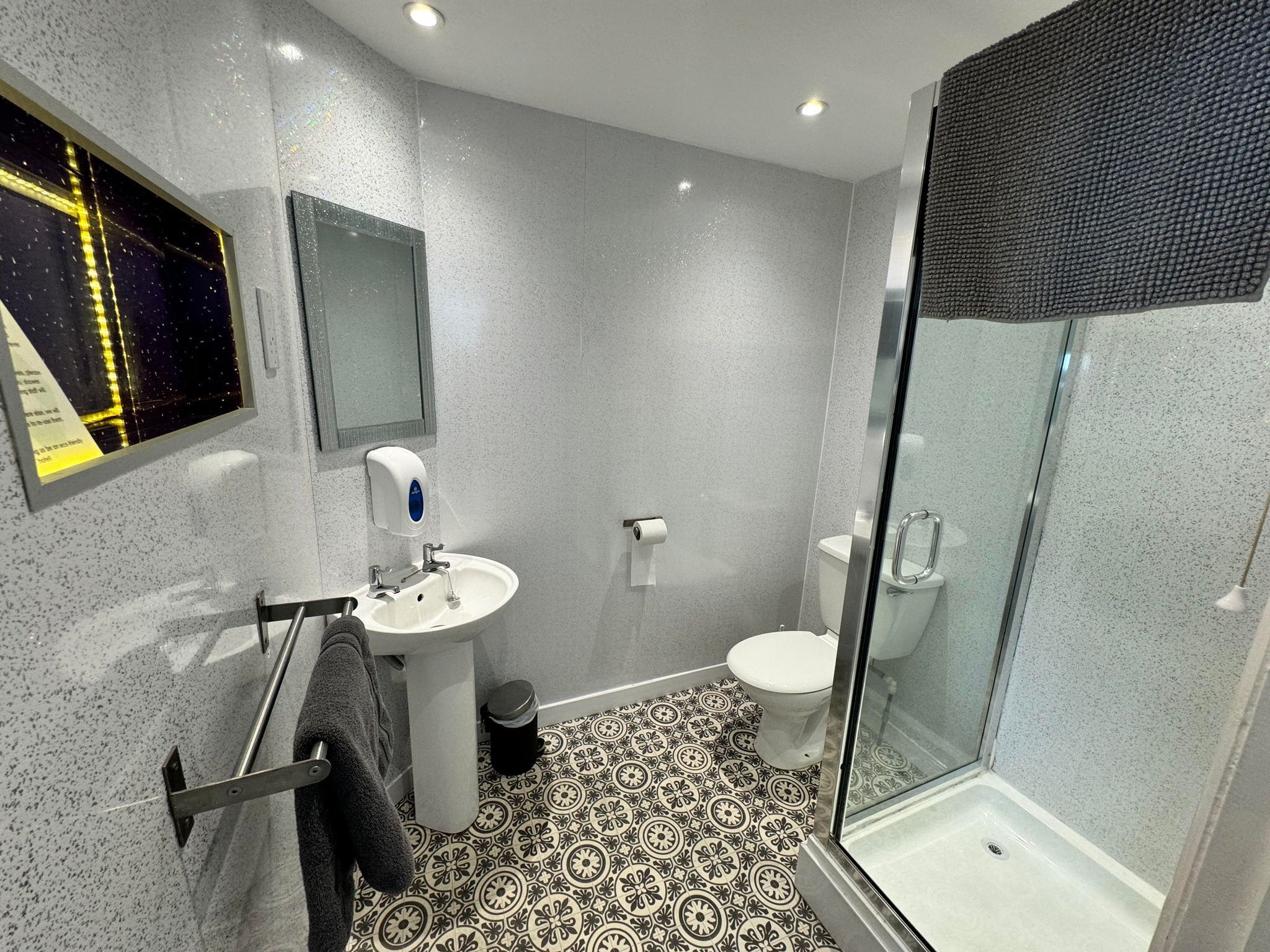 Un baño moderno con cabina de ducha de vidrio, lavamanos pedestal y retrete.