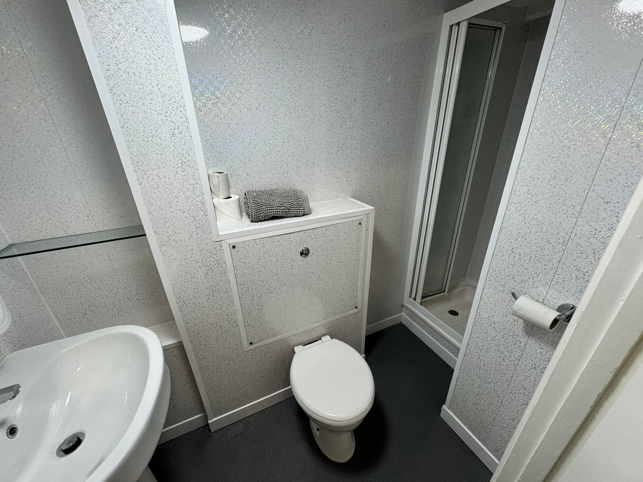 Un baño pequeño con inodoro blanco, lavamanos y cabina de ducha.