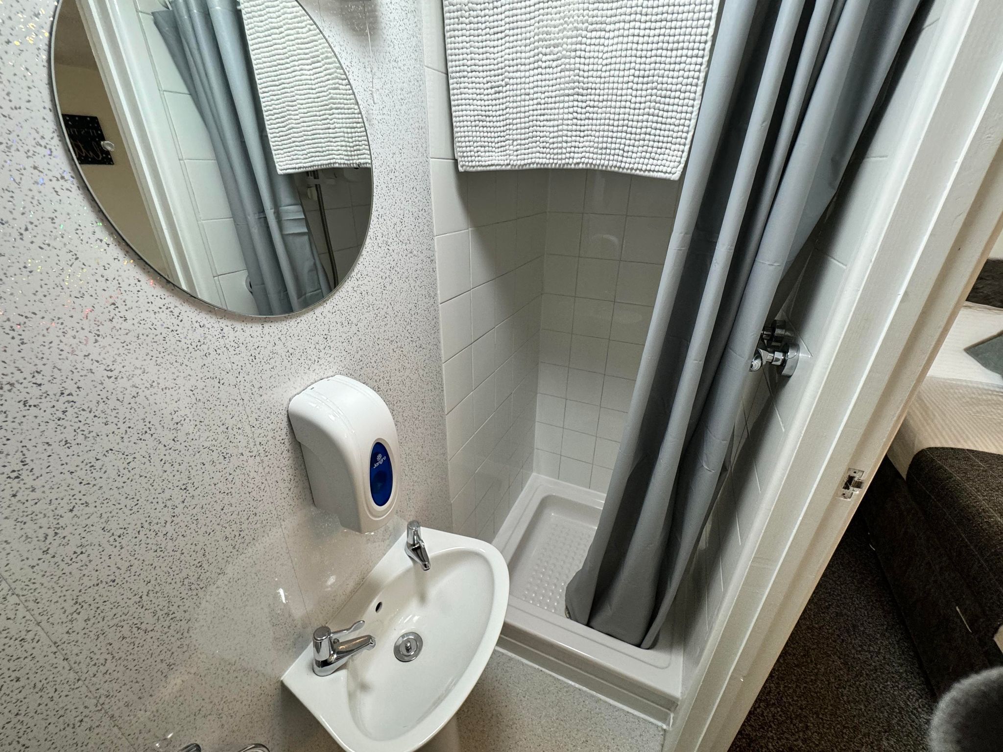 A bathroom with a white sink, a mirror, a towel dispenser, and a shower curtain.