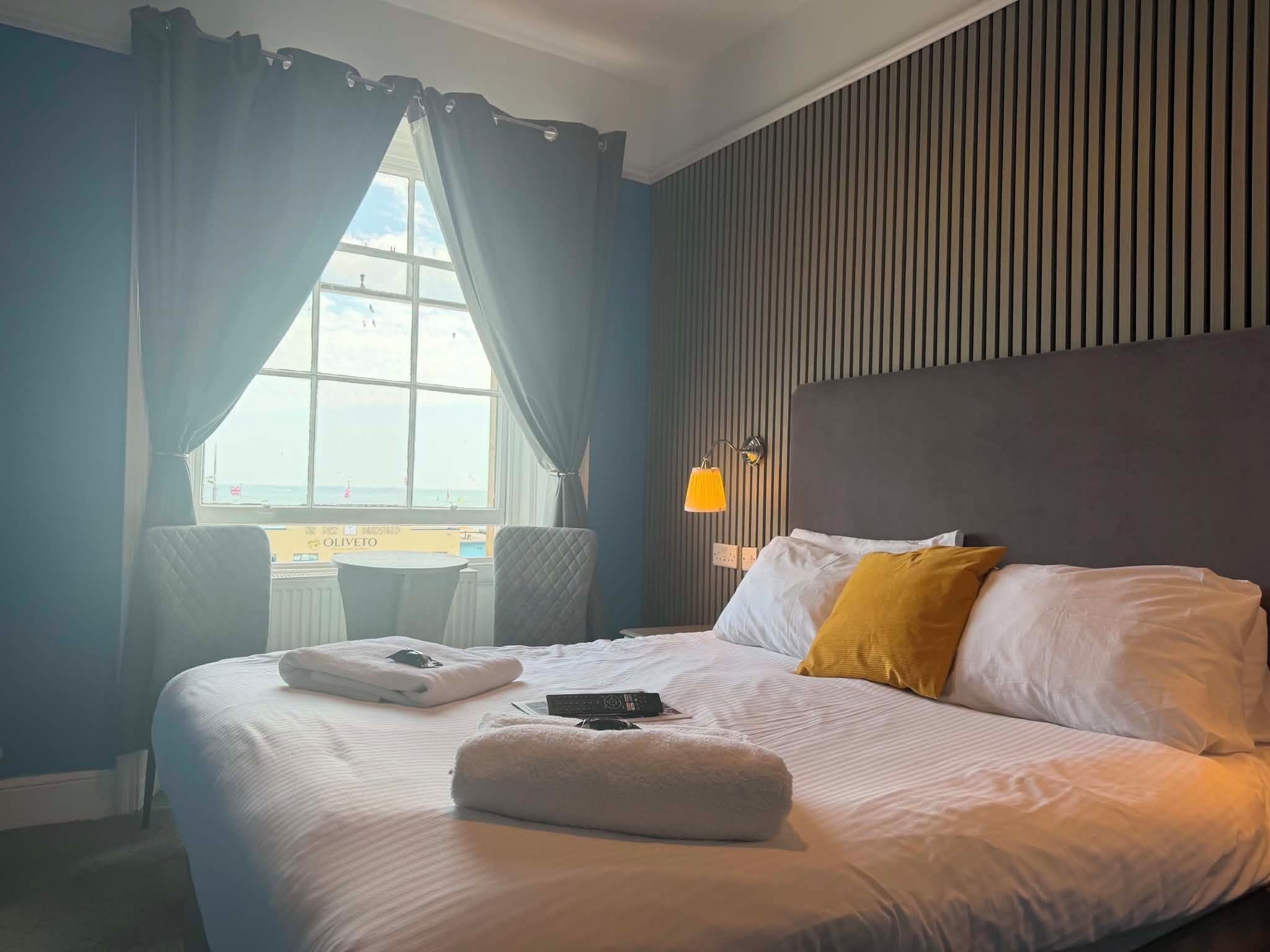 A hotel room with a large bed, a window with curtains, a bedside table, and a lamp.