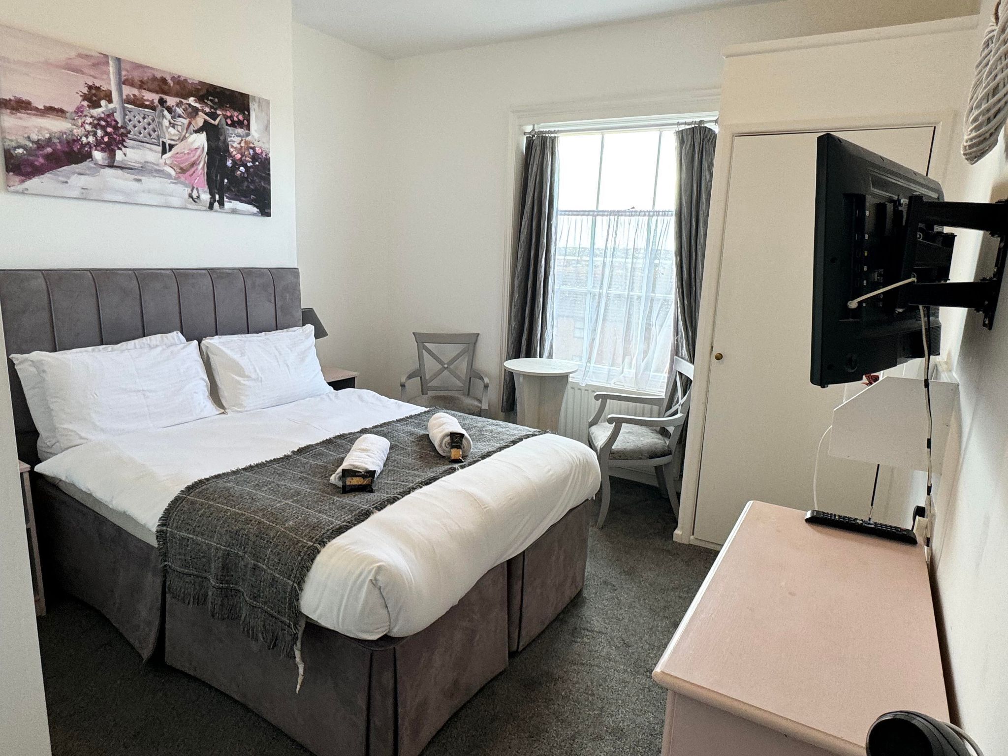 A hotel room with a bed, a desk, a chair, a TV, and a window with curtains.