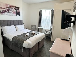 Habitación de hotel con cama, escritorio, silla, televisor y ventana con cortinas.