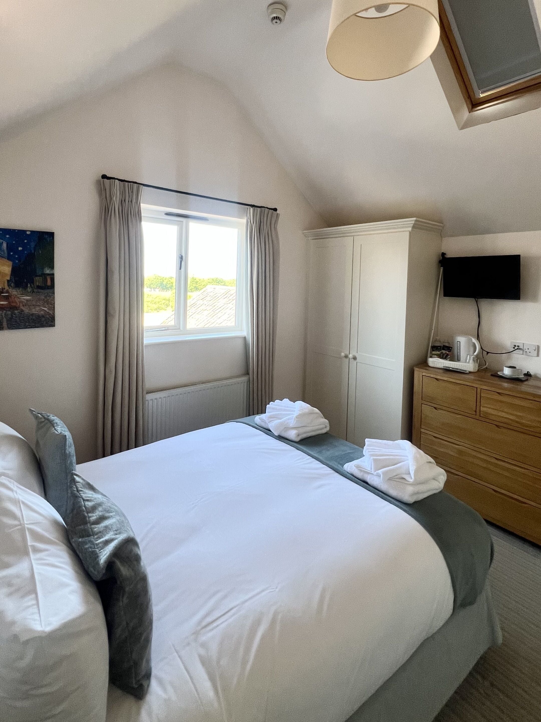 A hotel room with a bed, a dresser, a television, and a window with curtains.