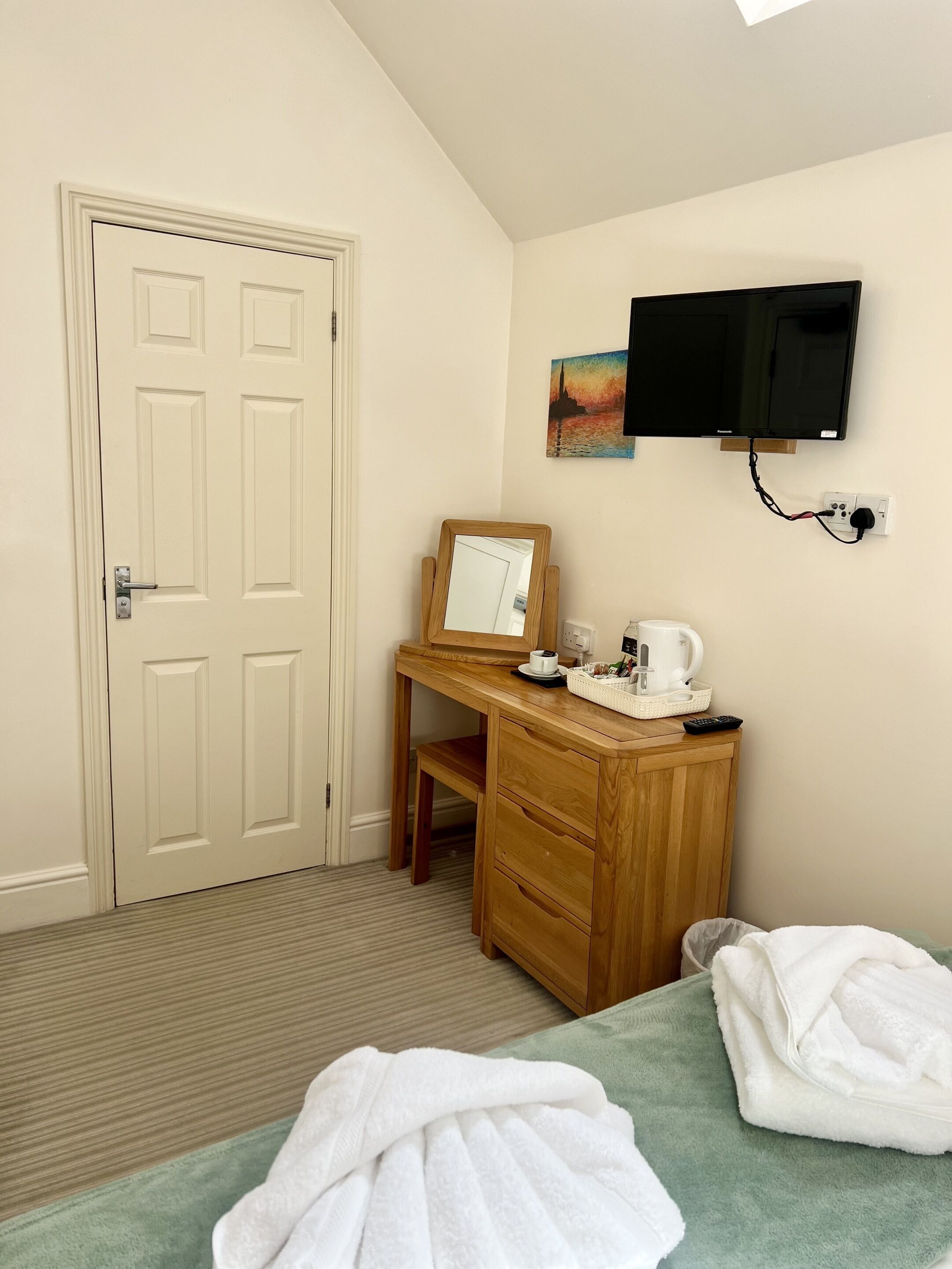 Habitación de hotel con escritorio de madera, televisor montado en la pared, una puerta y dos camas con toallas.