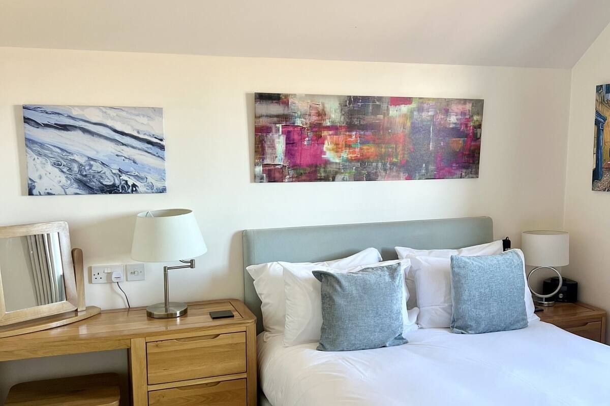 A neatly arranged hotel room with a bed, bedside tables, a desk, and two paintings on the wall.
