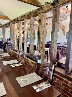 A long wooden table with metal chairs, set against a brick wall with exposed wooden beams. - The Parson Woodforde (Norwich)