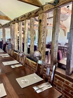 A long wooden table with metal chairs, set against a brick wall with exposed wooden beams.