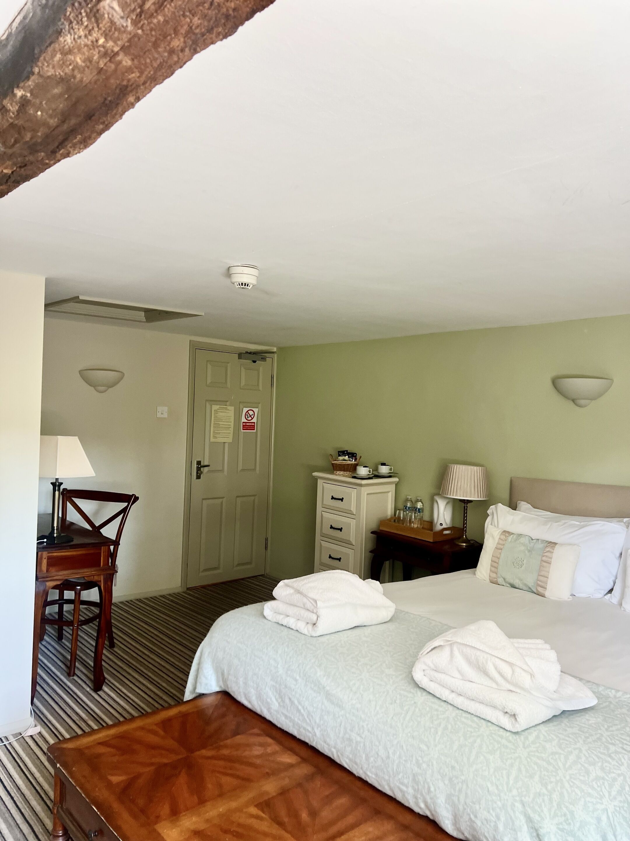 Une chambre d’hôtel comprenant un lit, un bureau, une chaise, une commode et une lampe.