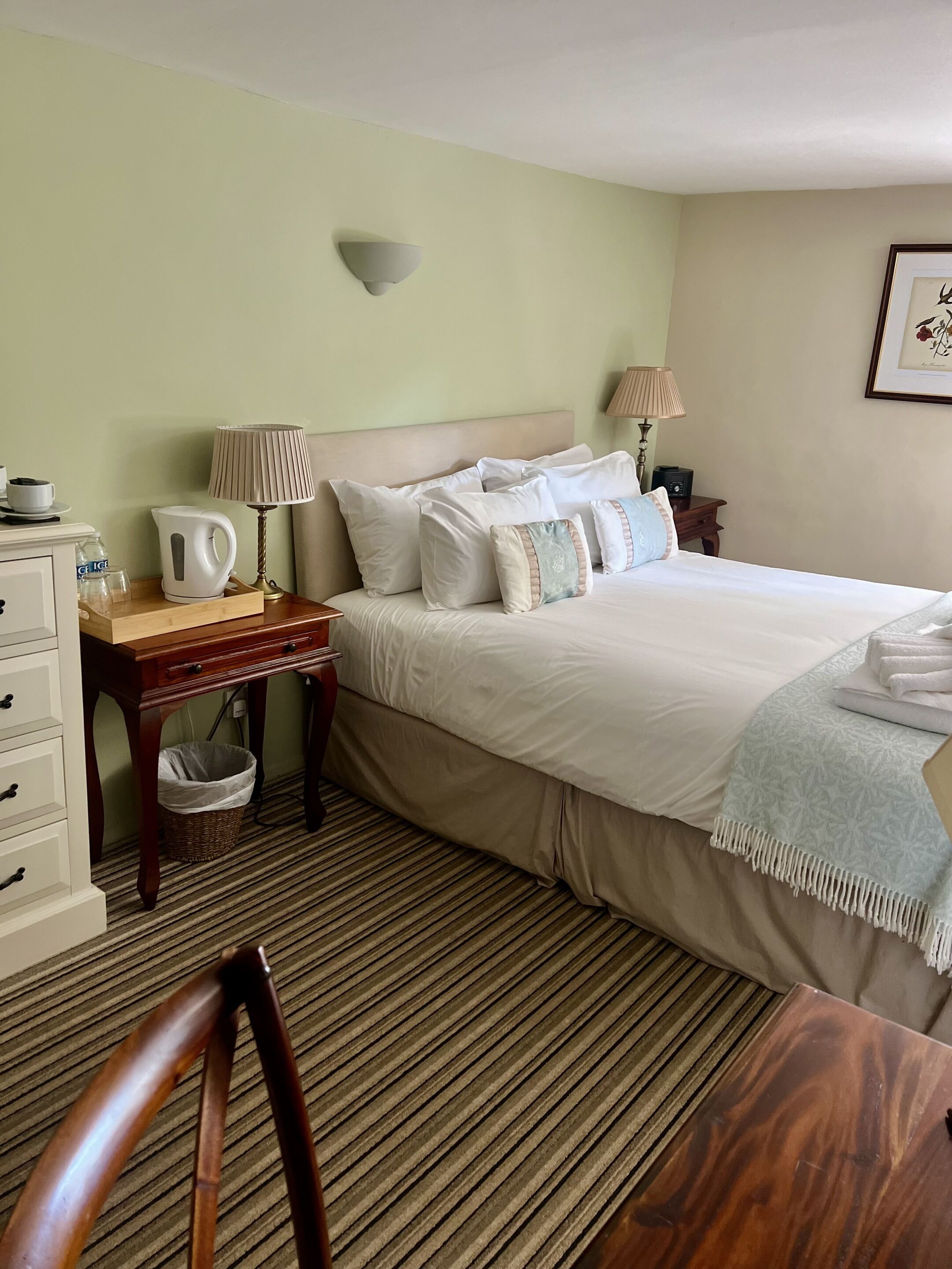Une chambre d’hôtel bien rangée, avec un lit, des tables de chevet, une lampe, une bouilloire et une corbeille à déchets.