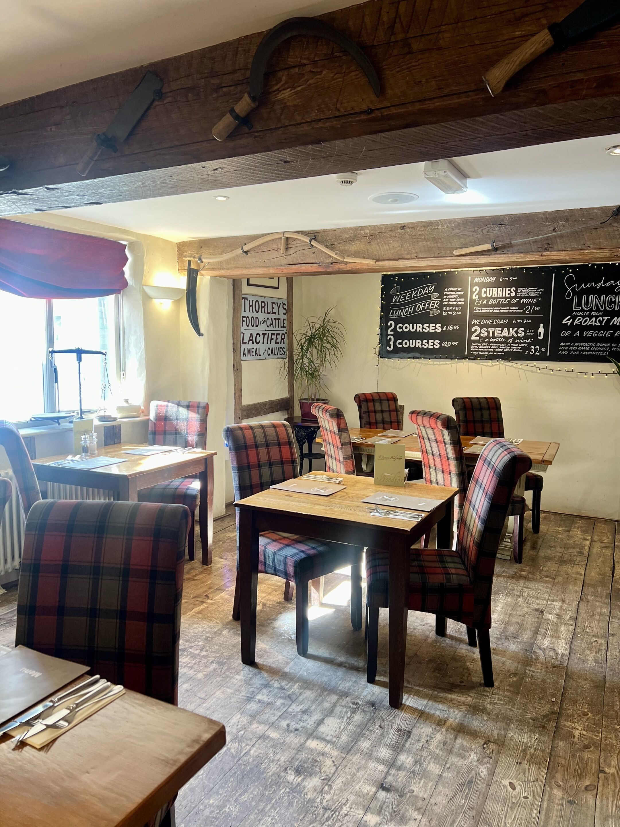 A restaurant interior with wooden tables and plaid chairs, a chalkboard menu, and a rustic ceiling.