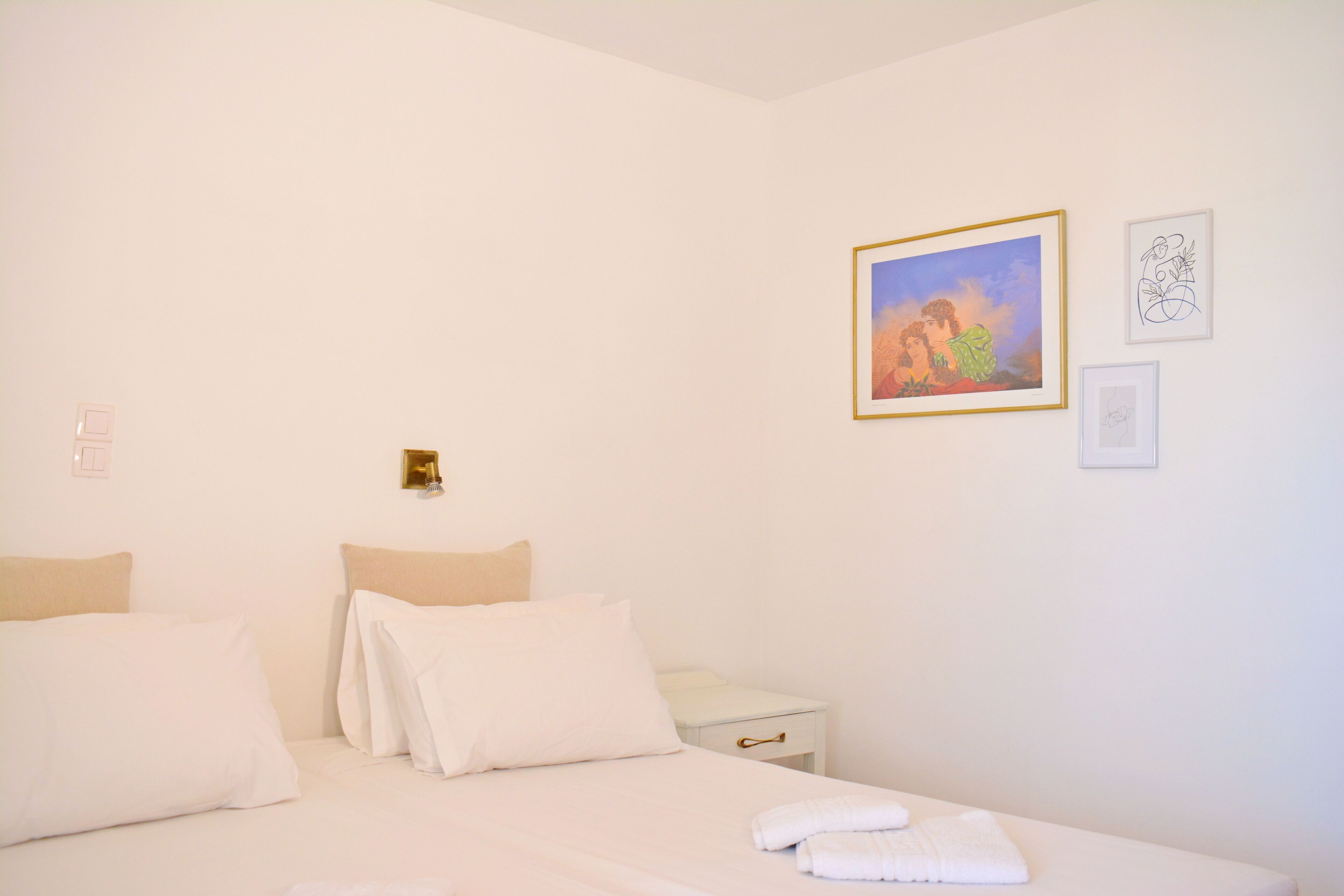 A hotel room with a bed, a nightstand, and a wall with framed artwork.