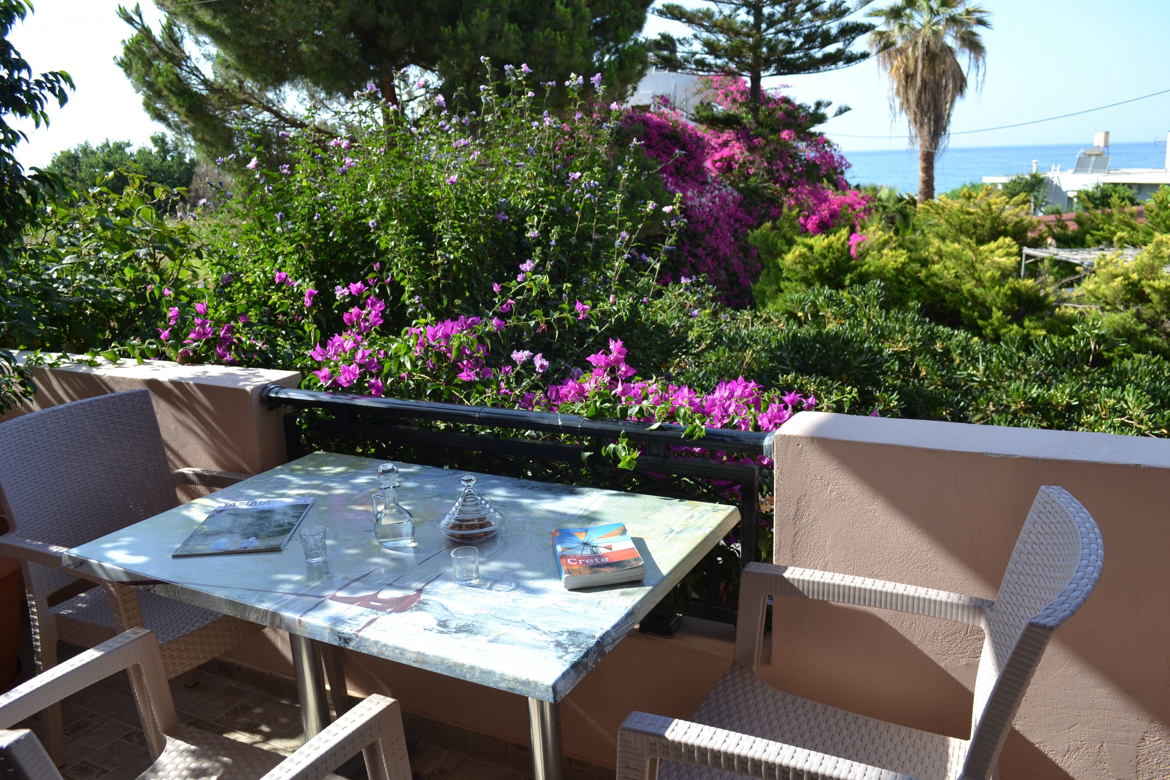 An outdoor patio with a table and chairs, surrounded by lush greenery and vibrant flowers.