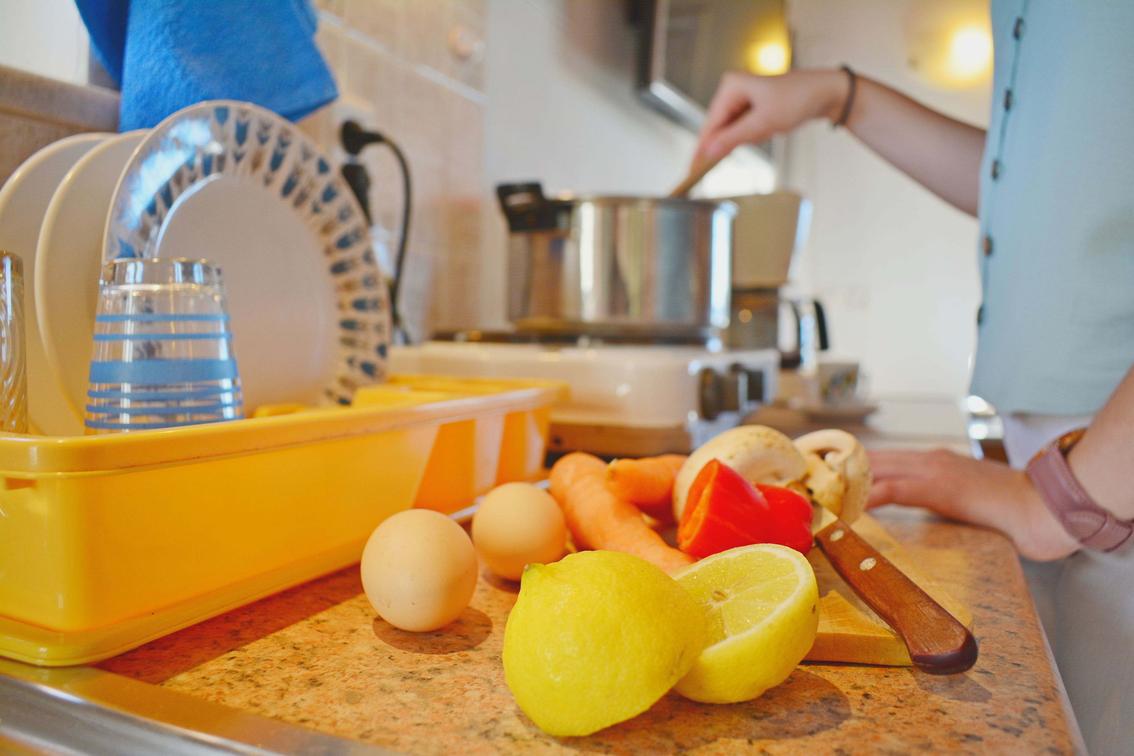 A kitchen counter with a dish rack, eggs, carrots, and a lemon.