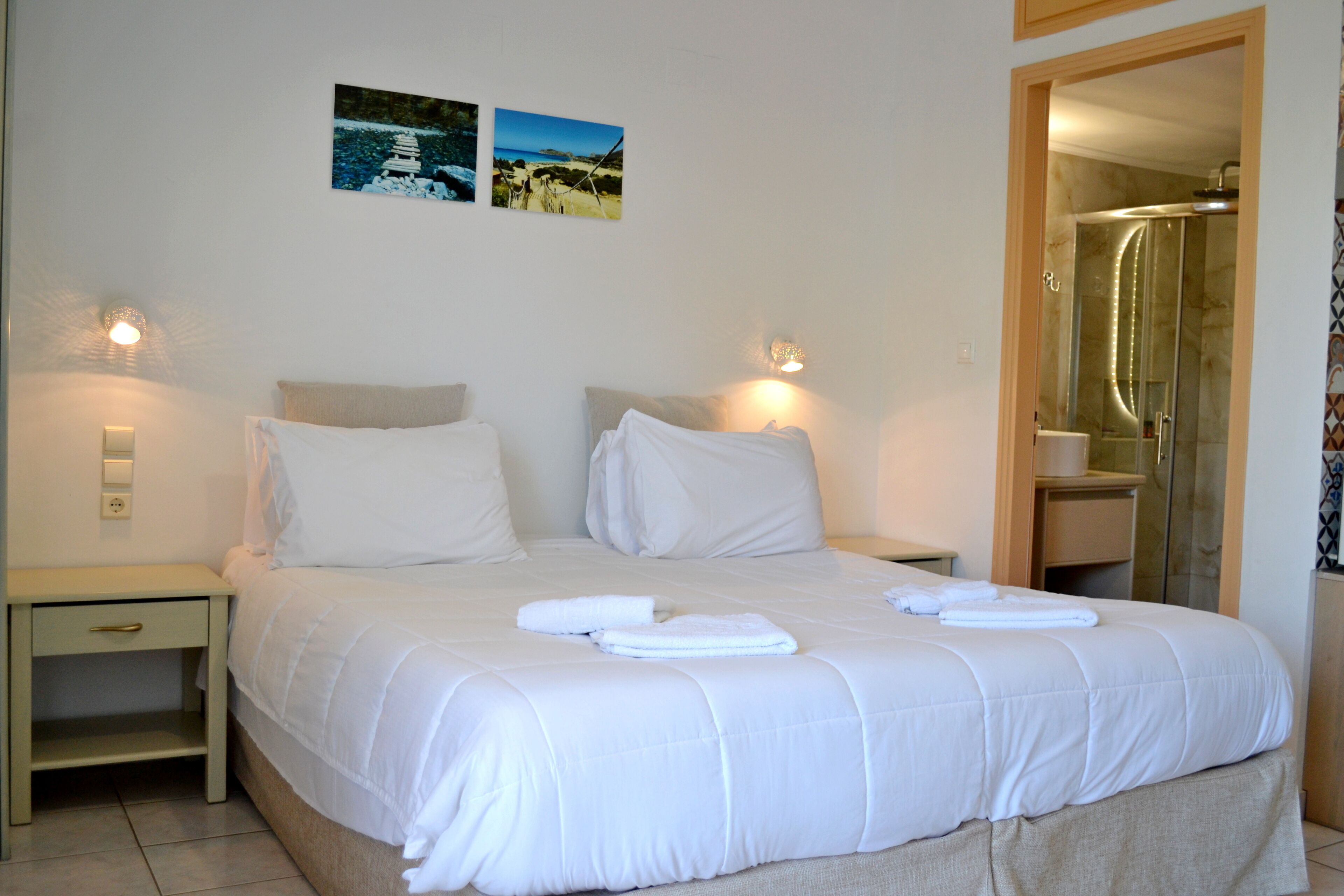 A neatly made bed with white linens, two bedside tables with lamps, and a glass shower door.