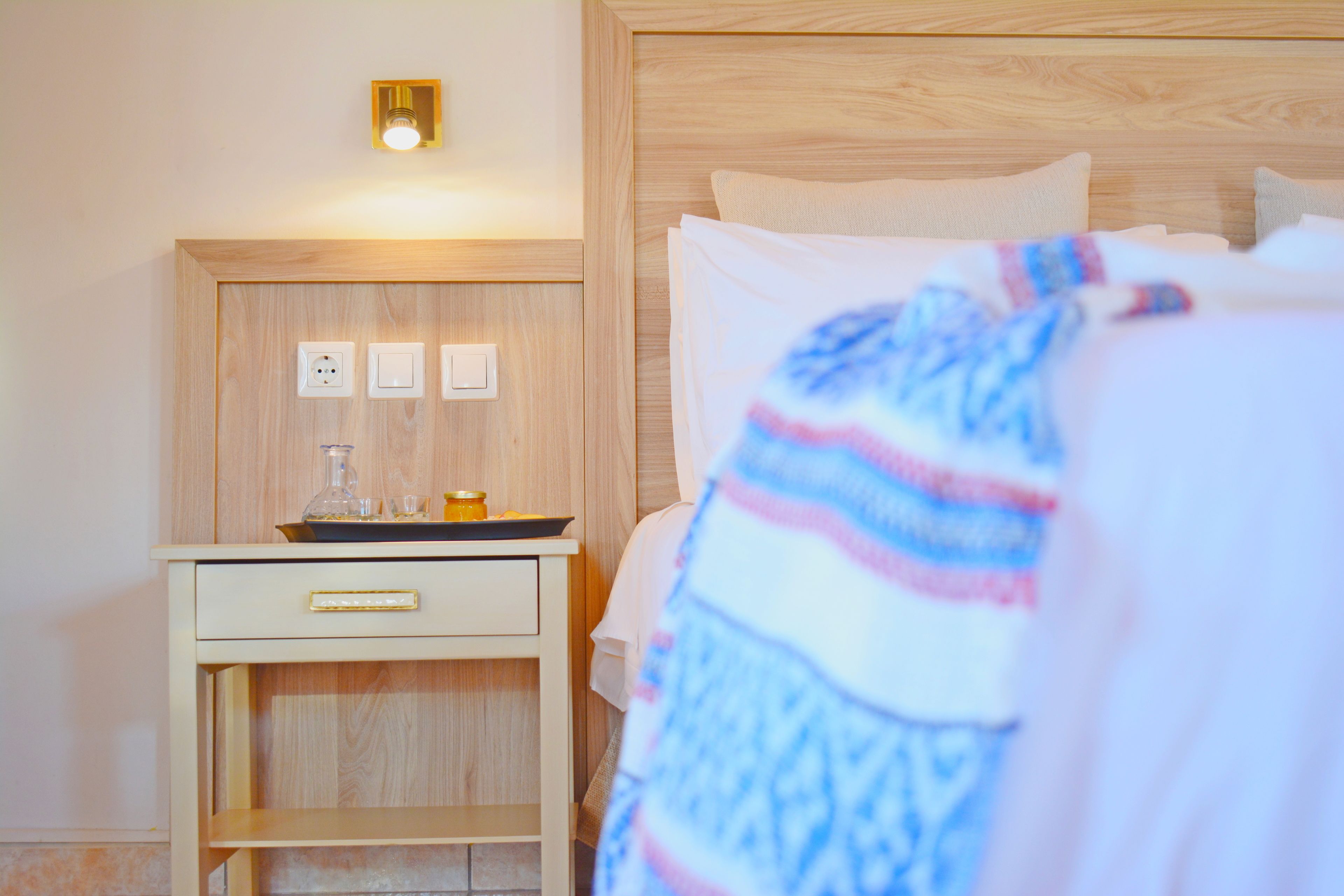 A hotel room with a wooden headboard, a bedside table with a lamp, and a bed with a striped blanket.