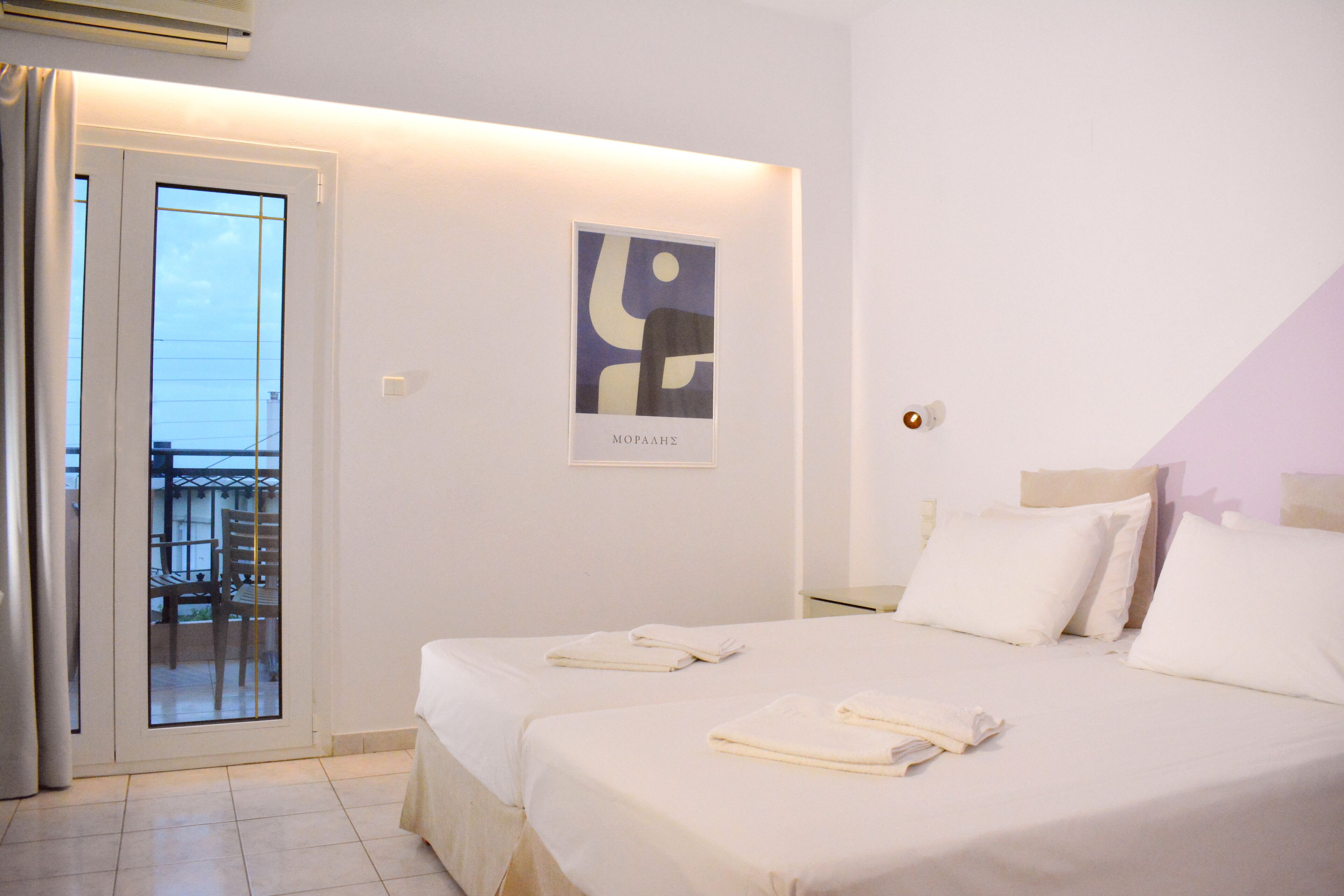 Camera d'albergo con due letti, un balcone e un quadro astratto appeso al muro.